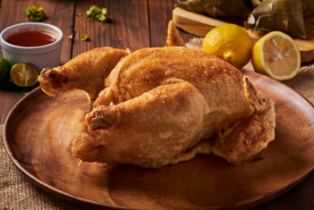 Appetizing photo of a whole Lechon Manok (Filipino roasted chicken) or batter-fried whole chicken preparation on a wooden board.