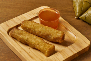 Two crispy fried ngoiong served with dipping sauce on a wooden plate.